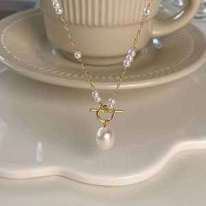 Detail of elegant gold OT toggle necklace with natural pearls on a white ceramic dish