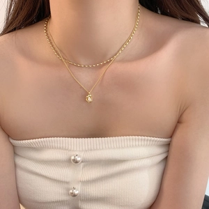 Close-up of a double-layered gold necklace with a baroque pearl on a woman's collarbone