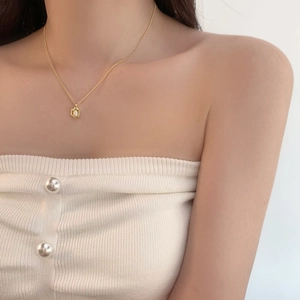 Detail of freshwater pearl pendant necklace with gold irregular bezel on white outfit