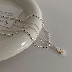 Detail of a layered silver necklace featuring a natural pearl on a sleek ceramic plate