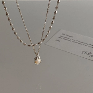 Close-up of double-layered silver necklace with freshwater pearl pendant and olive chain