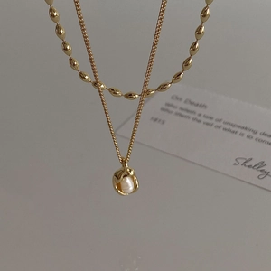 Detail of layered gold necklace with baroque pearl pendant and olive bead chain