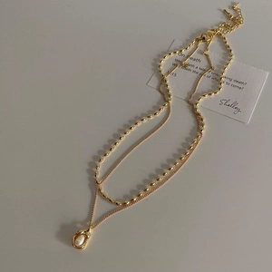 Detail of gold layered necklace featuring a freshwater pearl pendant on a beige surface
