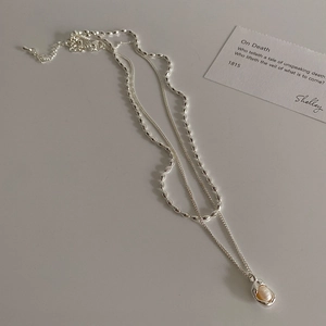 Detail of layered silver necklaces featuring a natural baroque pearl pendant on a card
