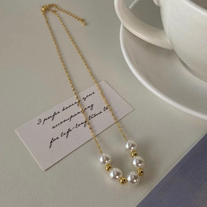 Detailed shot of a gold-plated pearl necklace with five round white beads and lobster clasp