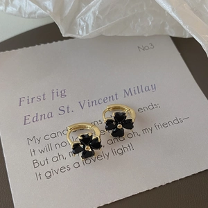 Detail of clover earrings with black heart petals on golden hoops over vintage paper
