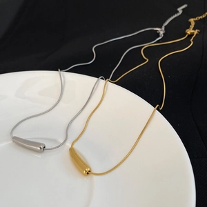 Nahaufnahme minimalistischer Schlangenketten in Gold und Silber mit Tropfenanhängern