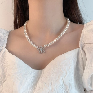Collier ras du cou en perles avec pendentif fleur en diamants porté par un mannequin femme