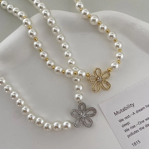 Vue détaillée du collier de perles avec pendentif fleur et zircon sur plateau céramique