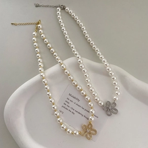 Colliers de perles dorées et argentées avec pendentifs fleurs en strass sur plateau blanc