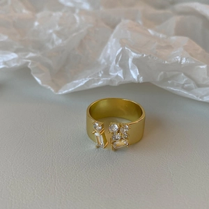 Close-up of golden open ring featuring asymmetrical zircon stone clusters on a textured surface