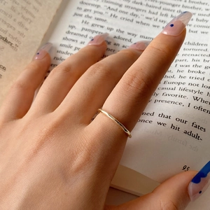Minimalist wavy gold open ring on a model's hand with warm aesthetic lighting