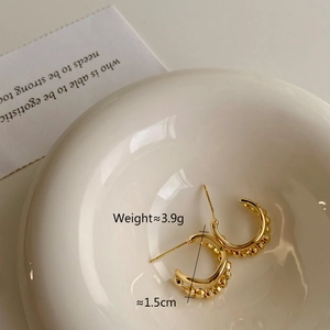Detail view of 1.5cm golden C-shaped hoop earrings with textured beads on ceramic bowl