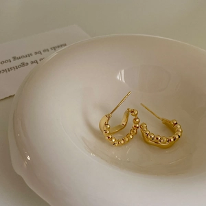 Detail of irregular C-shaped gold beaded earrings on a white ceramic plate