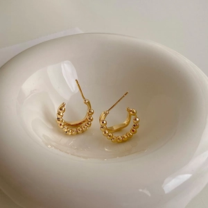 Macro view of gold beaded C-shaped hoop earrings showcasing intricate metal texture