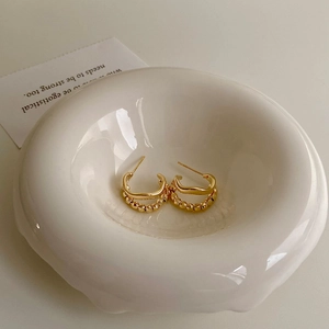 Detail of gold double-layer earrings with wavy lines and beaded texture in a ceramic bowl