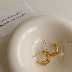 Detail of gold irregular C-shaped hoop earrings with beaded edges on a ceramic plate