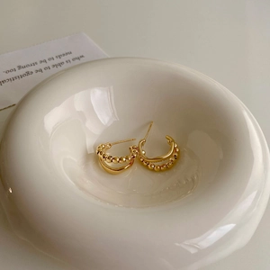 Irregular C-shaped gold hoop earrings with double-layered intertwined texture in ceramic bowl