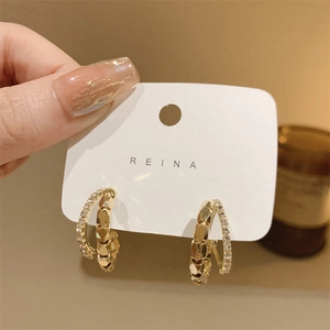 Close-up of golden double-layer hoop earrings with sparkling zircons on REINA card