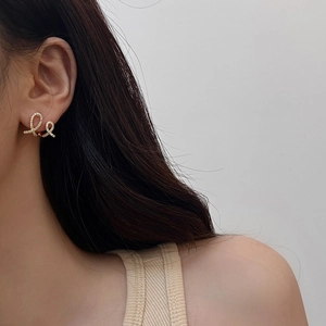 Detail shot of golden zircon earrings with a twisted crossover design on a model ear
