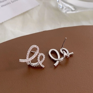 Macro detail of asymmetric spiral earrings with pink cubic zirconia on leather surface