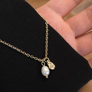 Detail of natural freshwater pearl and gold plated oval charm on a fine cable chain necklace