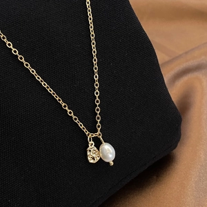 Close-up of gold chain with irregular lava pendant and a white baroque pearl on black stand