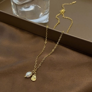 Detail of natural freshwater pearl and textured gold pendant on a minimalist chain