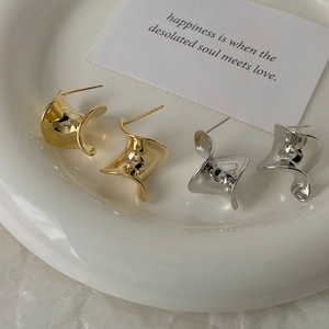 Macro detail of twisted sculptural stud earrings in polished gold and silver finishes