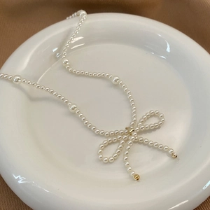 Détail du collier de perles crème avec un pendentif nœud en perles tissées main