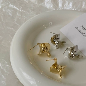 Minimalist twisted metal hoop earrings in gold and silver finish on a white tray