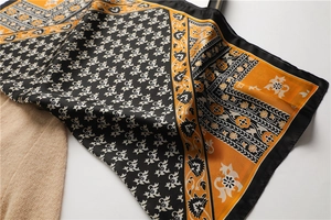 Détail d'un foulard en soie vintage aux motifs floraux noirs et orange sur tricot