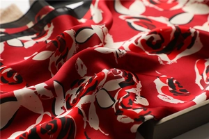 Detail shot of silk scarf with red rose pattern showing glossy texture and fabric sheen