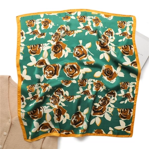 Retro green satin scarf with orange roses and white leaves laid on a beige cardigan