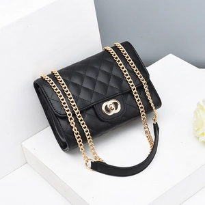 Sac bandoulière matelassé noir avec chaîne dorée exposé sur un socle blanc minimaliste