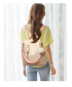 Detail of beige waterproof backpack with pink straps and a white fluffy ball pendant accessory