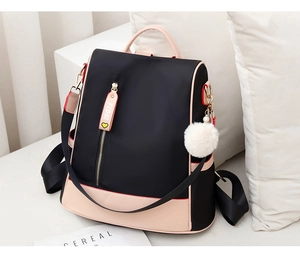 Close-up of black oxford backpack with pink leather trim and soft white pom-pom charm