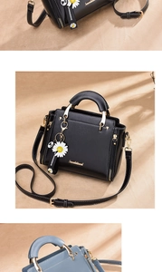 Detail of black faux leather handbag with golden hardware and daisy charm accessory