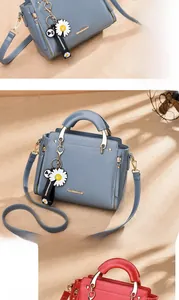 Detail of trendy handbag with daisy charm, metal handles and detachable strap in red and grey