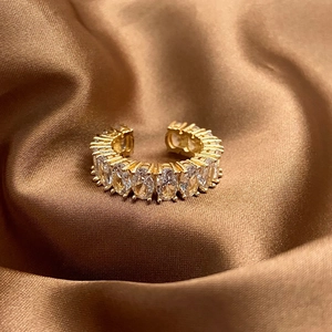 Dettaglio anello dorato regolabile con zirconi ovali su sfondo di raso marrone chic