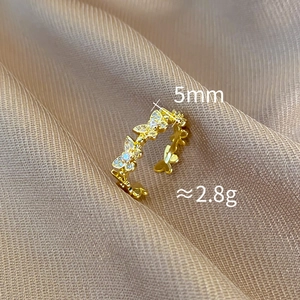 Close-up of gold butterfly ring with white zircons on champagne silk fabric, 5mm width