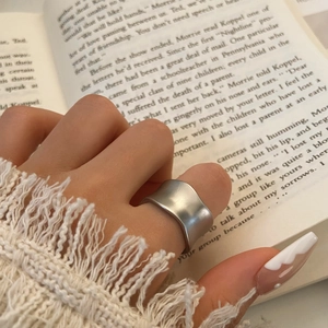 Vue macro d'une bague large argentée mate au design ondulé portée au doigt