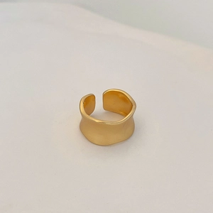 Détail macro d'une bague large en or mat avec bords ondulés irréguliers et texture