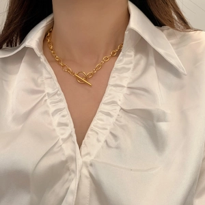 Détail d'un collier grosse chaîne dorée avec fermoir OT sur une chemise en satin blanc