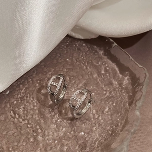 Close-up of silver H-shaped hoop earrings with micro-pave zircons on a glass tray