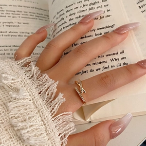 Dettaglio dell'anello incrociato placcato oro con zirconi indossato davanti a un libro