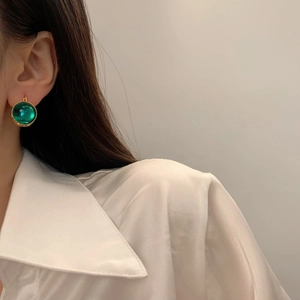 Gros plan d'un mannequin portant des boucles d'oreilles en verre vert avec bords dorés