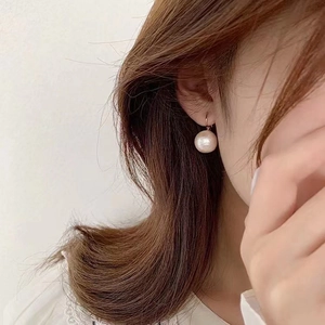 Close-up of a 10mm round cotton pearl earring with gold hook on a female model