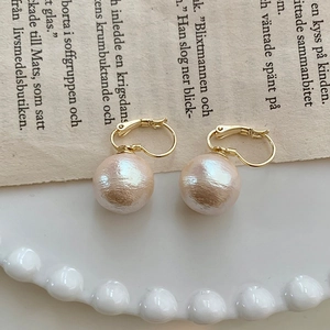 Macro detail of large pink cotton pearl earring with gold-plated clasp on vintage paper