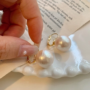 Macro detail of French retro cotton pearl earrings with textured gold plated hooks